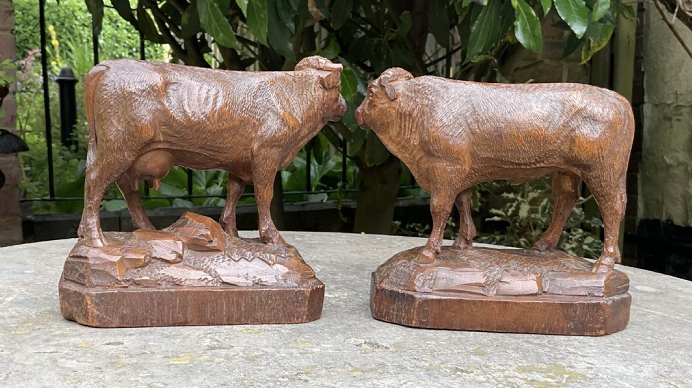 A pair of hand-carved wooden sculptures depicting a bull and a cow standing on naturalistic carved bases with artist signatures. View III