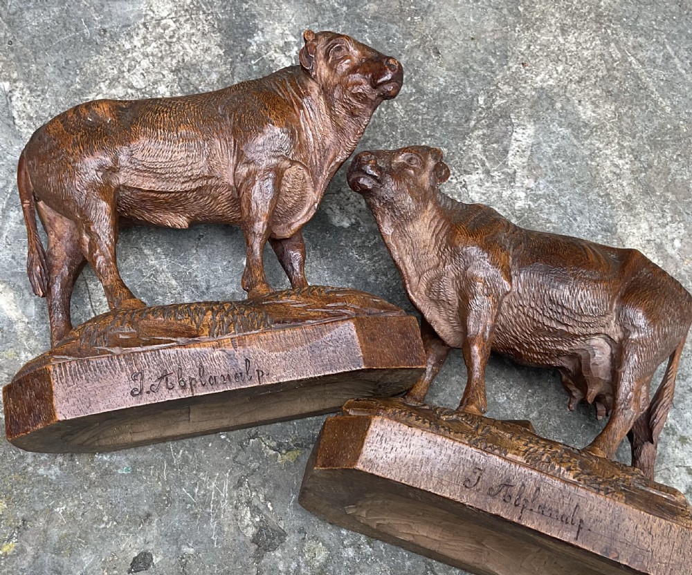 A pair of hand-carved wooden sculptures depicting a bull and a cow standing on naturalistic carved bases with artist signatures. View VII