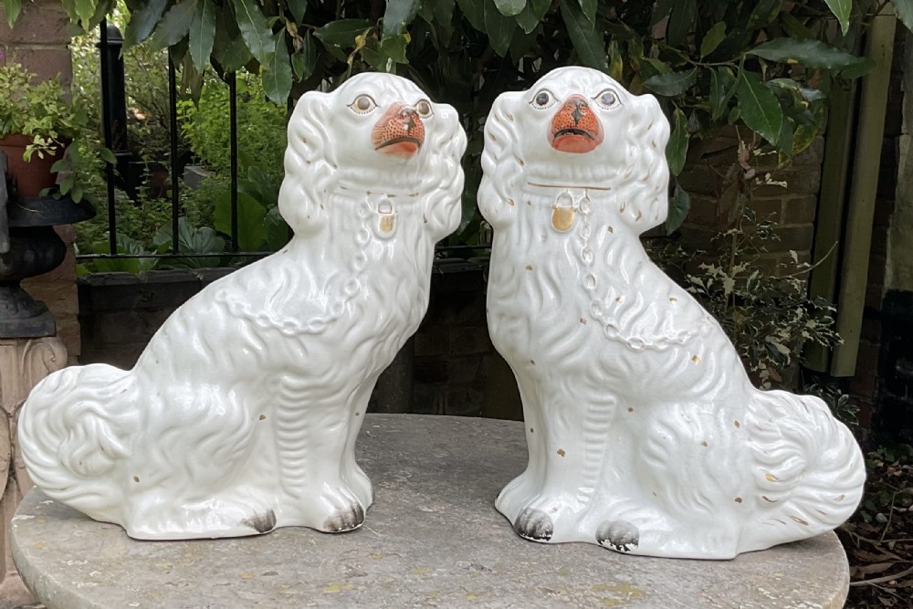 A pair of seated Victorian white earthenware Staffordshire spaniel figurines decorated with gilded chains and painted muzzles.