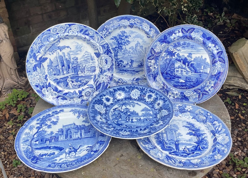 A set of six circular Georgian blue and white transferware earthenware plates decorated with pastoral scenes, classical ruins, and intricate floral borders.