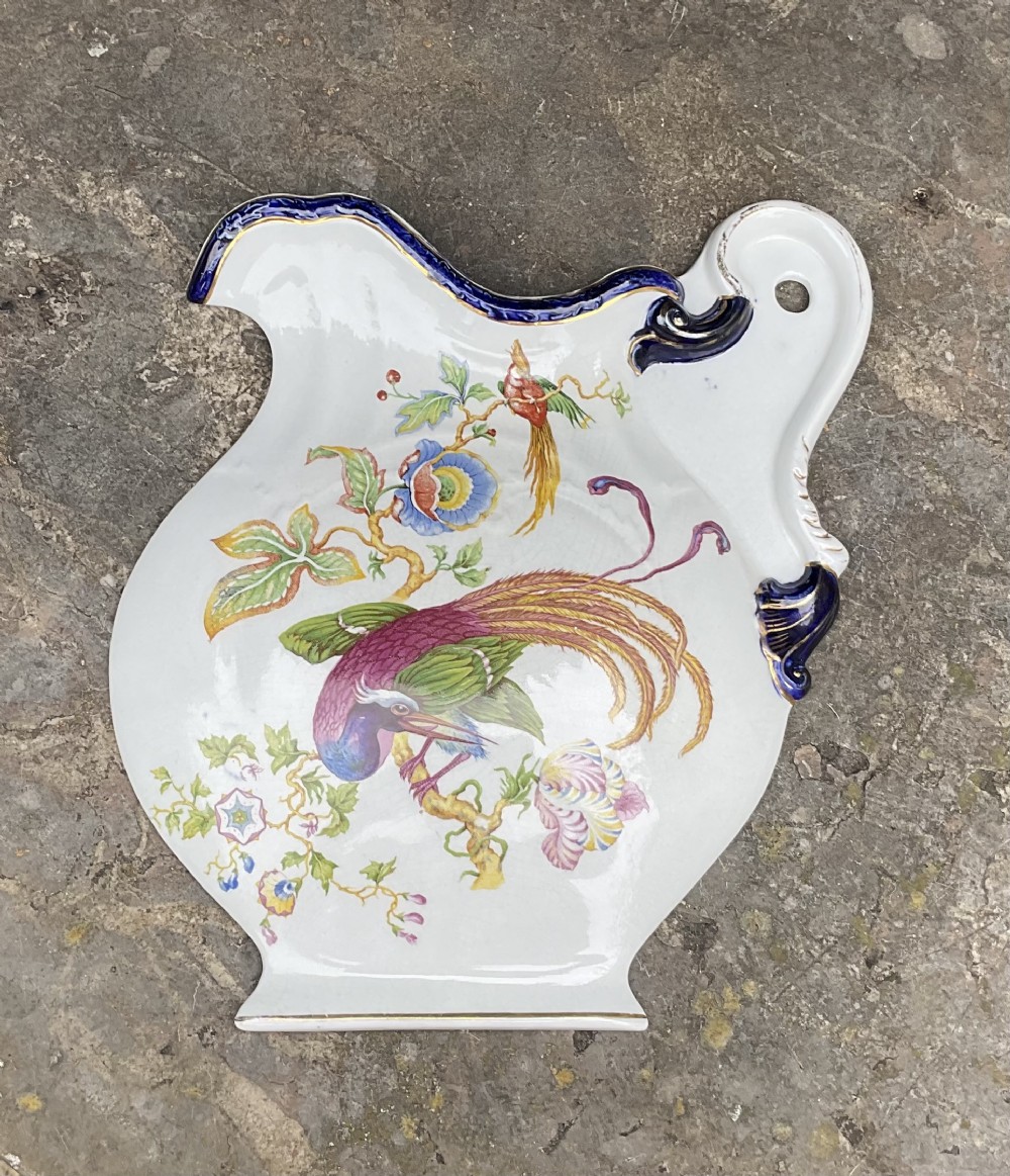 A flat Victorian earthenware plaque shaped like a jug with a painted exotic bird on a floral branch, cobalt blue scroll rim, and gilded accents.