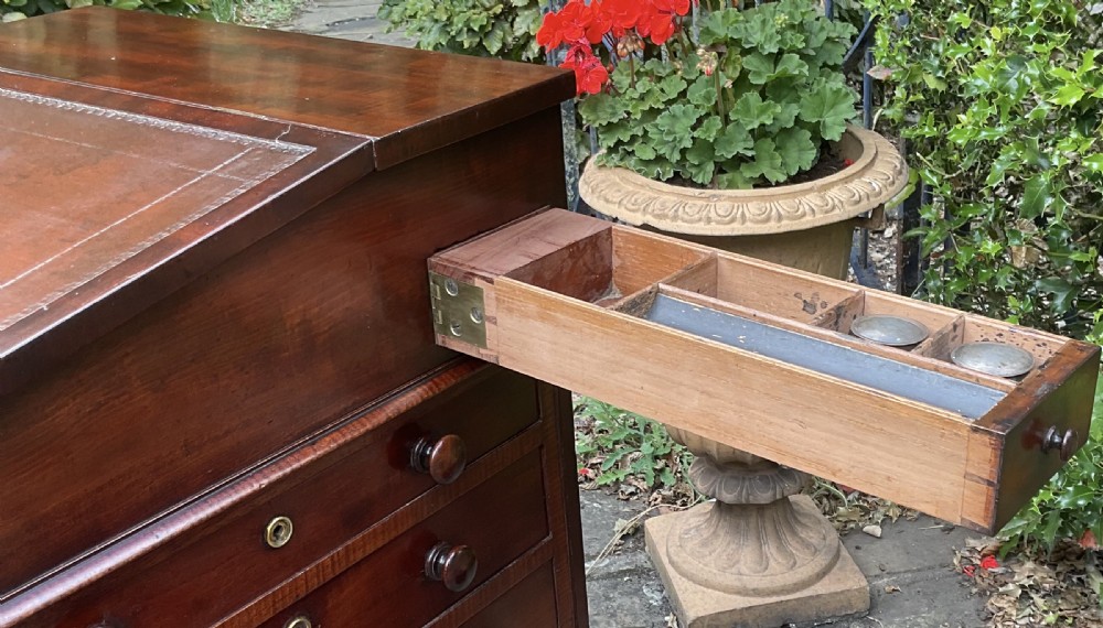 A Regency mahogany Davenport desk featuring an inclined leather-lined writing slope, carved fan spandrels, flame mahogany panel sides, and vertical side drawers with turned handles. View VII