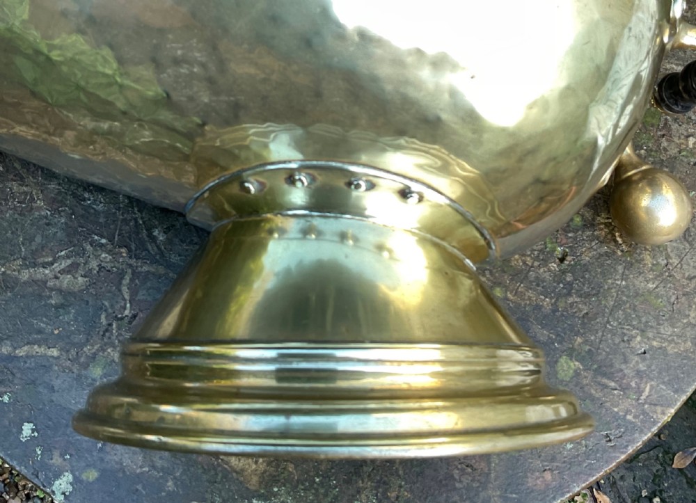 A Victorian brass coal helmet scuttle resting on a pedestal base, complete with an ebonised wooden handle and a matching brass scoop. View XIV