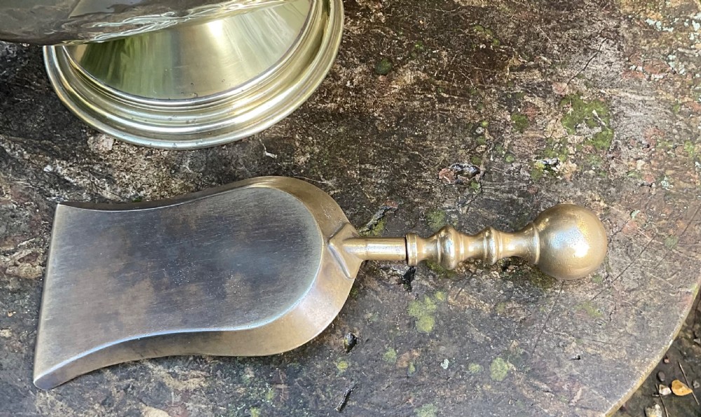 A Victorian brass coal helmet scuttle resting on a pedestal base, complete with an ebonised wooden handle and a matching brass scoop. View XVII