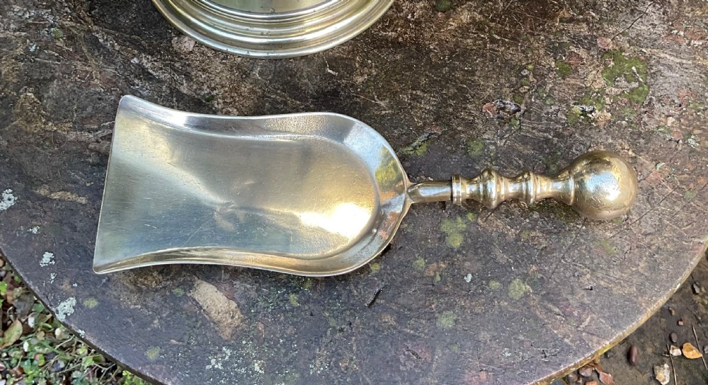 A Victorian brass coal helmet scuttle resting on a pedestal base, complete with an ebonised wooden handle and a matching brass scoop. View XVIII