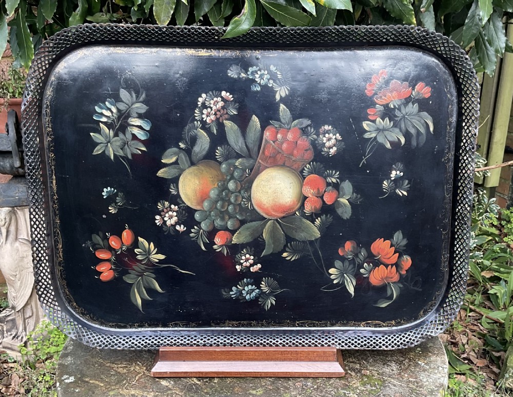 A rectangular black lacquered toleware tray featuring a central handpainted fruit and floral motif surrounded by a pierced metal gallery border.