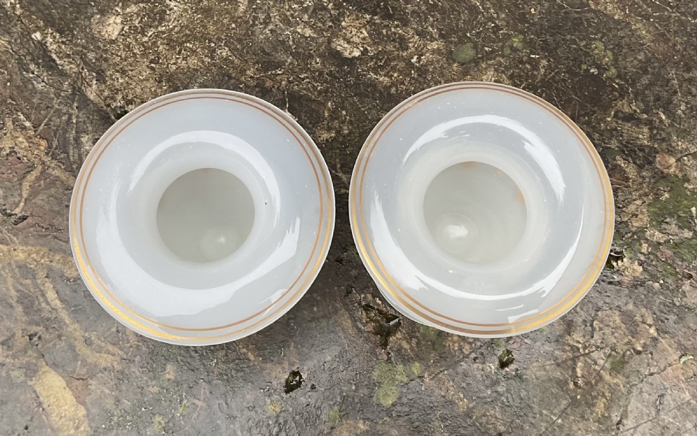 A pair of translucent white opaline glass urn-shaped vases featuring wide flared rims, turned pedestal stems, and delicate hand-painted gold leaf floral swags. View III