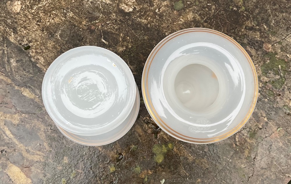 A pair of translucent white opaline glass urn-shaped vases featuring wide flared rims, turned pedestal stems, and delicate hand-painted gold leaf floral swags. View VI