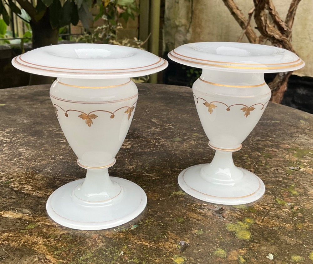 A pair of translucent white opaline glass urn-shaped vases featuring wide flared rims, turned pedestal stems, and delicate hand-painted gold leaf floral swags. View VII