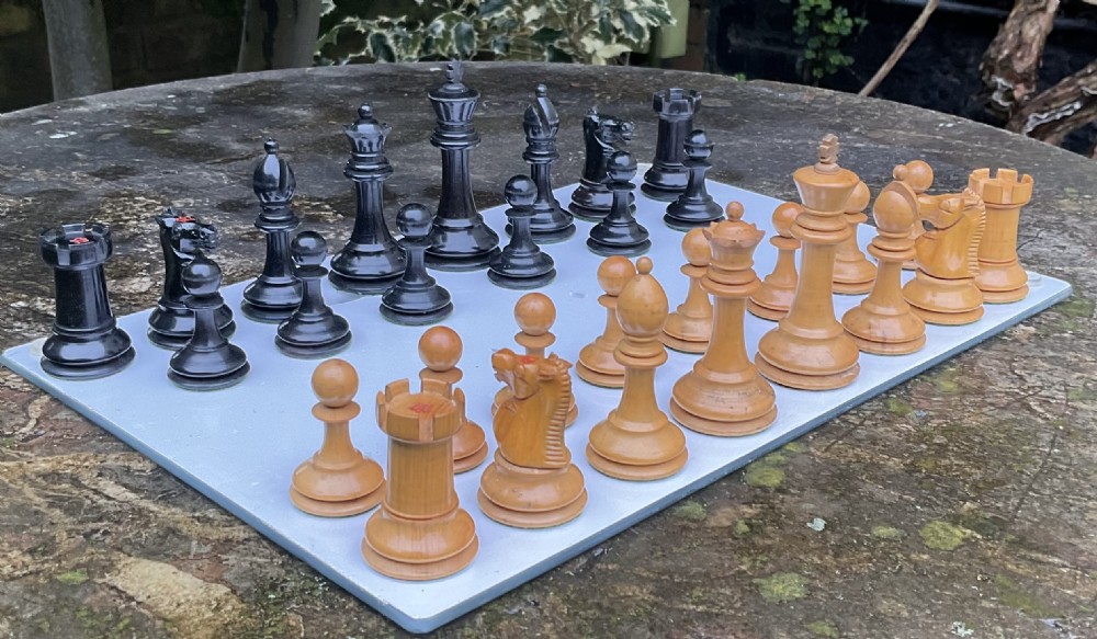 A complete set of turned and carved Staunton chess pieces crafted from light boxwood and black ebony, arranged on a surface.