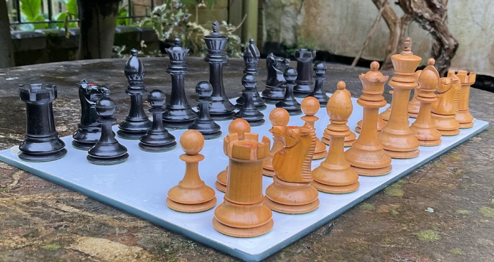 A complete set of turned and carved Staunton chess pieces crafted from light boxwood and black ebony, arranged on a surface. View IX