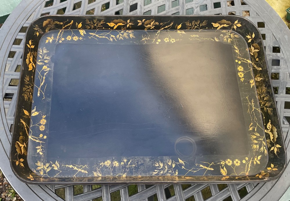 A large rectangular black lacquer papier-mache tray featuring rounded corners and a gilded floral border.