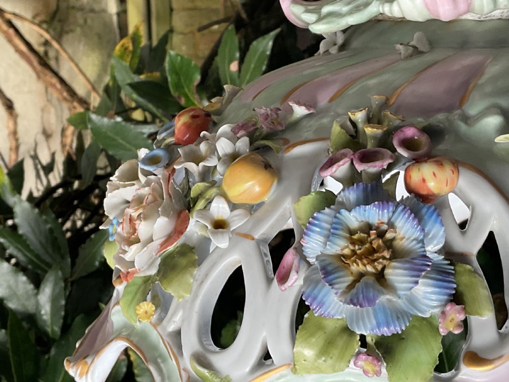 An ornate German porcelain centrepiece featuring a pierced lattice bowl encrusted with colourful three-dimensional flowers, supported by a central pedestal with a seated winged cherub on a scrollwork base. View XIII