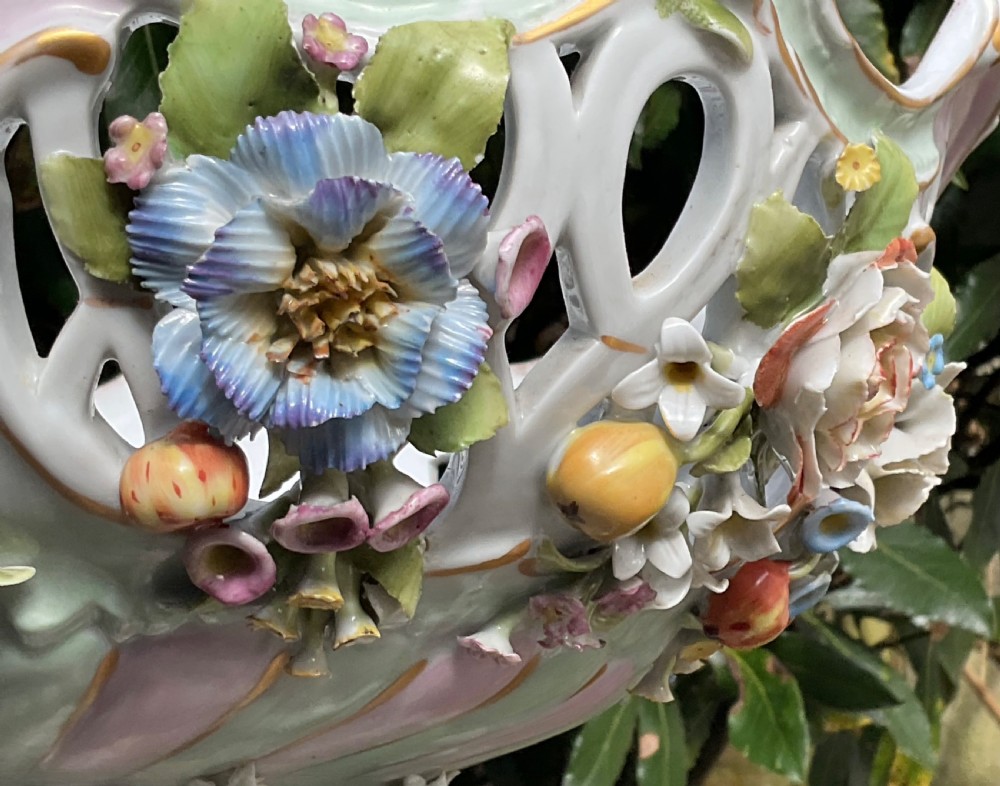 An ornate German porcelain centrepiece featuring a pierced lattice bowl encrusted with colourful three-dimensional flowers, supported by a central pedestal with a seated winged cherub on a scrollwork base. View XIV