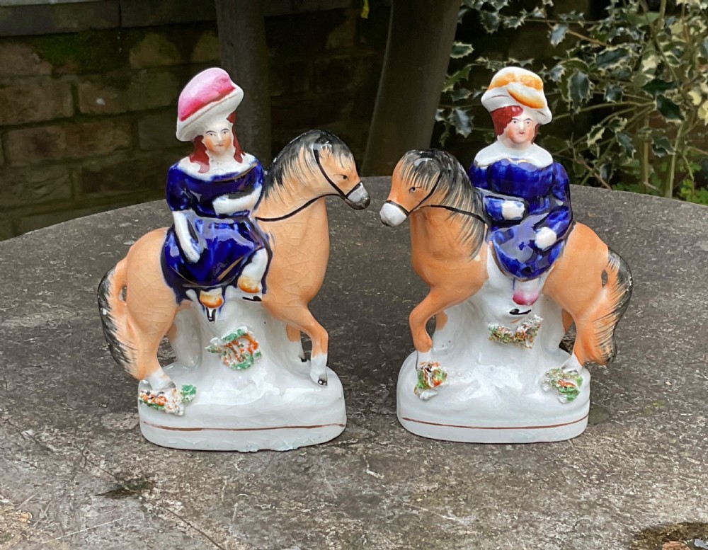A pair of antique Victorian Staffordshire ceramic figurines depicting children dressed in cobalt blue riding orange horses.