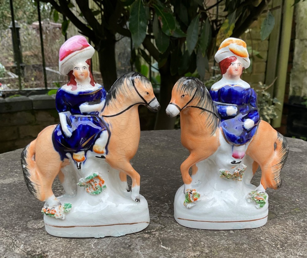 A pair of antique Victorian Staffordshire ceramic figurines depicting children dressed in cobalt blue riding orange horses. View VI