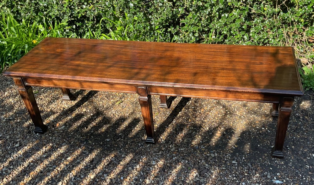 An Edwardian long polished mahogany window seat featuring a rectangular top and six tapered square legs with block details. View II