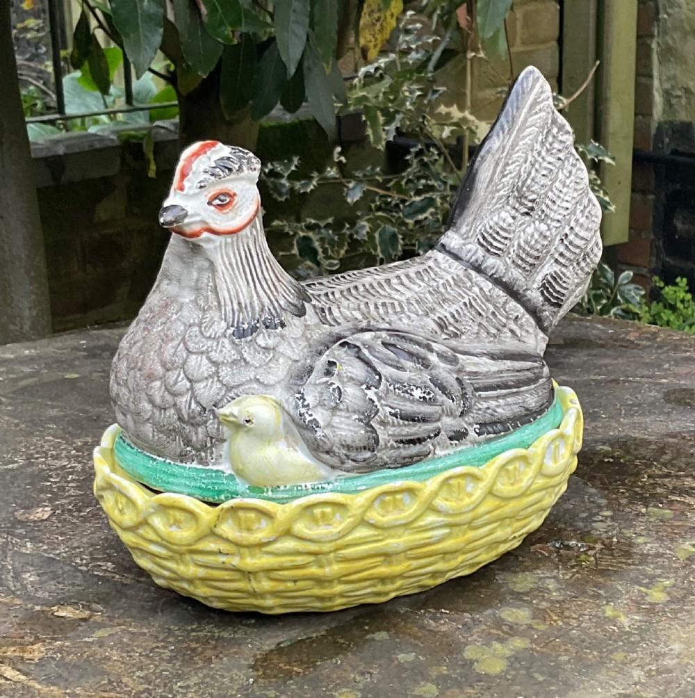 Victorian Staffordshire earthenware egg crock shaped like a grey hen with a chick sitting in a yellow woven basket nest.