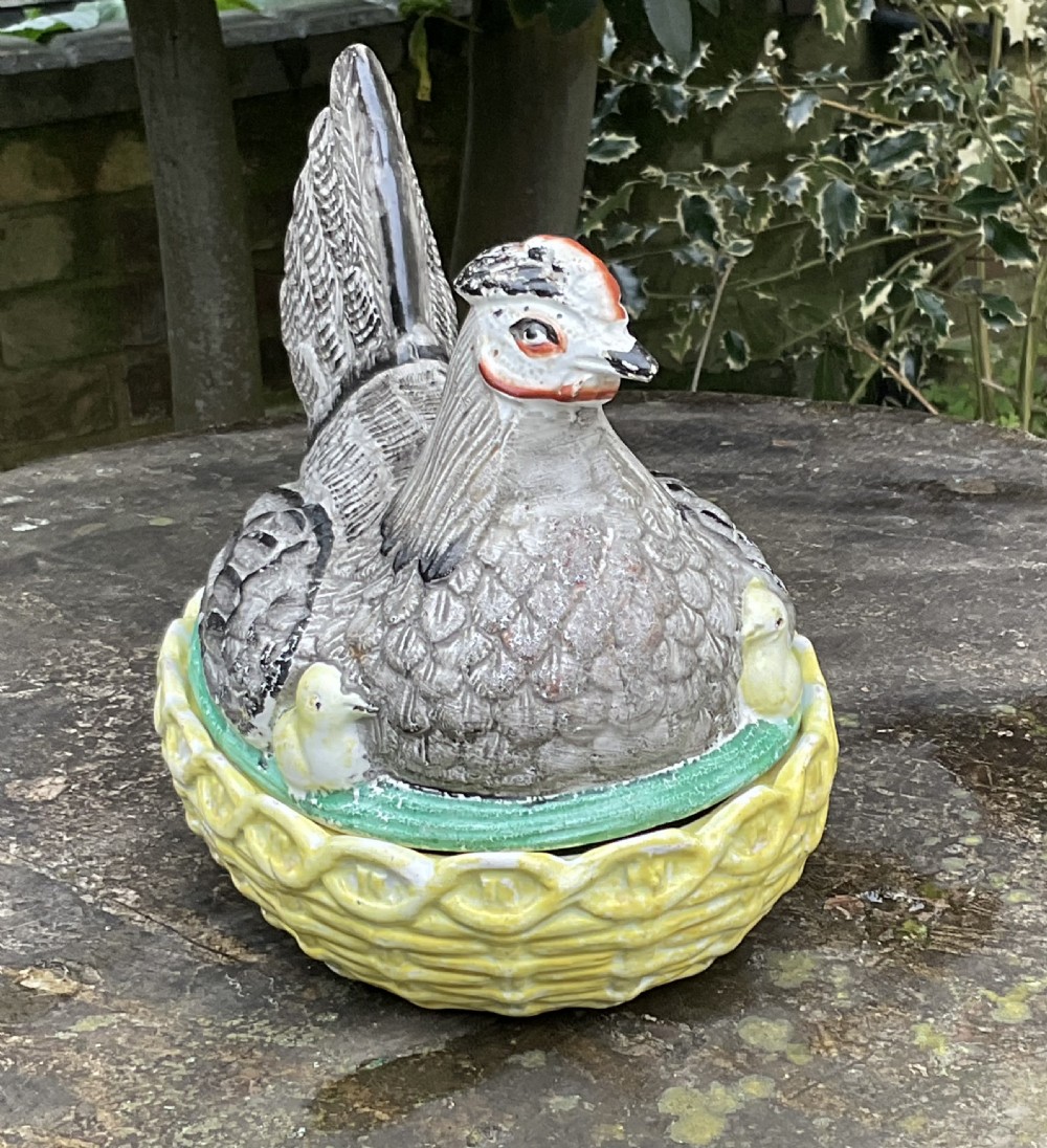 Victorian Staffordshire earthenware egg crock shaped like a grey hen with a chick sitting in a yellow woven basket nest. View II