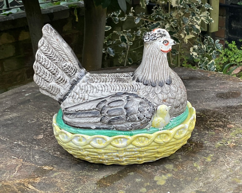Victorian Staffordshire earthenware egg crock shaped like a grey hen with a chick sitting in a yellow woven basket nest. View III