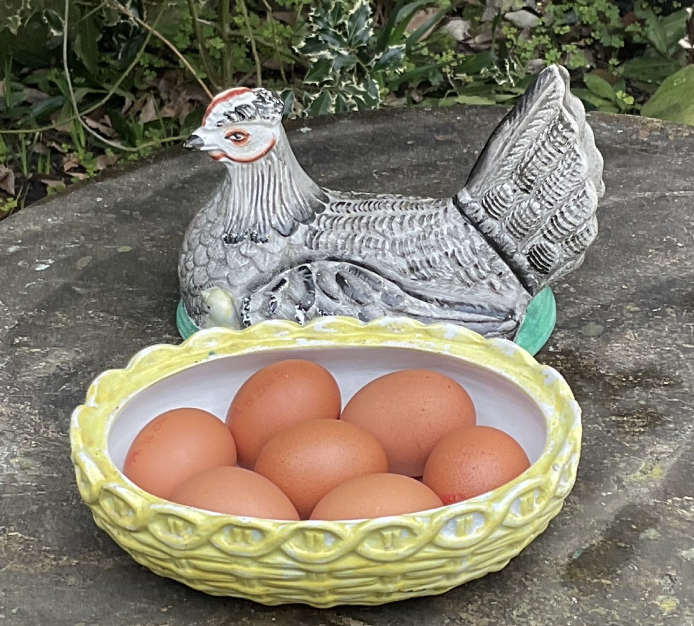 Victorian Staffordshire earthenware egg crock shaped like a grey hen with a chick sitting in a yellow woven basket nest. View IV