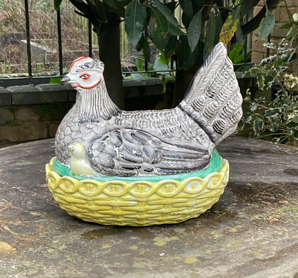Victorian Staffordshire earthenware egg crock shaped like a grey hen with a chick sitting in a yellow woven basket nest. View VII