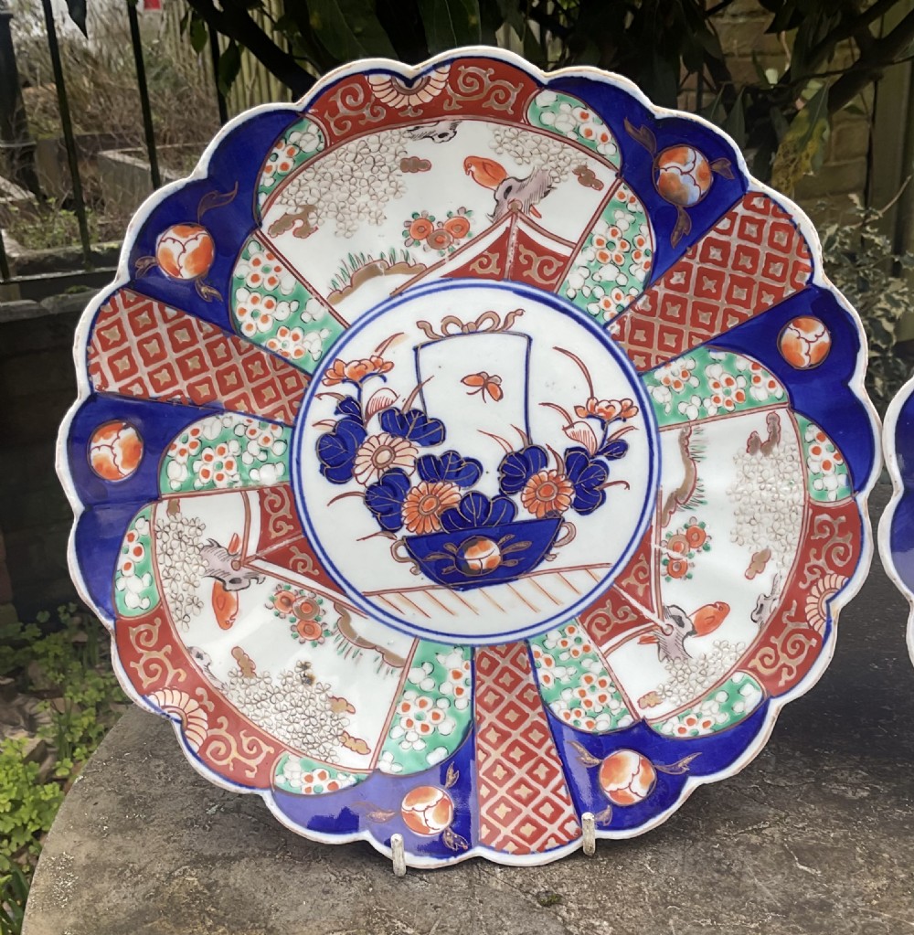 A pair of late nineteenth-century Japanese Imari porcelain plates featuring scalloped rims, painted in cobalt blue, rust red, and green with central floral basket motifs and patterned panel borders. View II