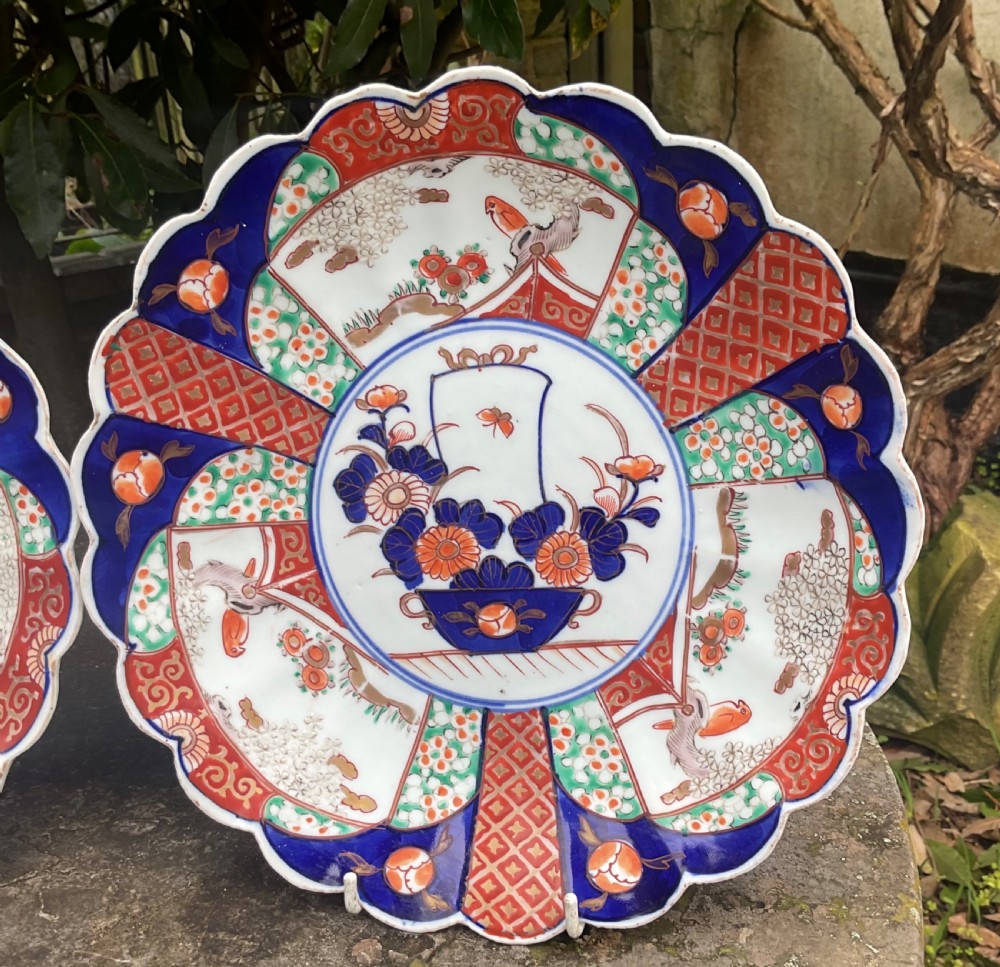 A pair of late nineteenth-century Japanese Imari porcelain plates featuring scalloped rims, painted in cobalt blue, rust red, and green with central floral basket motifs and patterned panel borders. View III