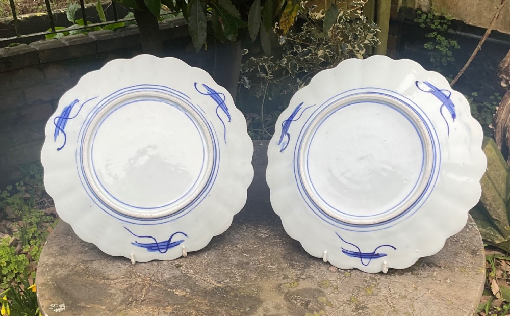 A pair of late nineteenth-century Japanese Imari porcelain plates featuring scalloped rims, painted in cobalt blue, rust red, and green with central floral basket motifs and patterned panel borders. View IV