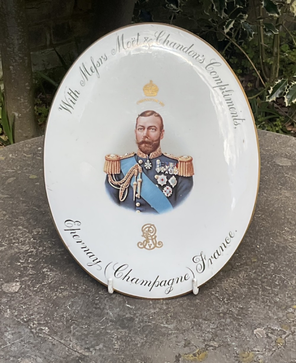 An oval white ceramic plaque featuring a central portrait of King George V in uniform with gold Moet & Chandon lettering and a gilded edge.
