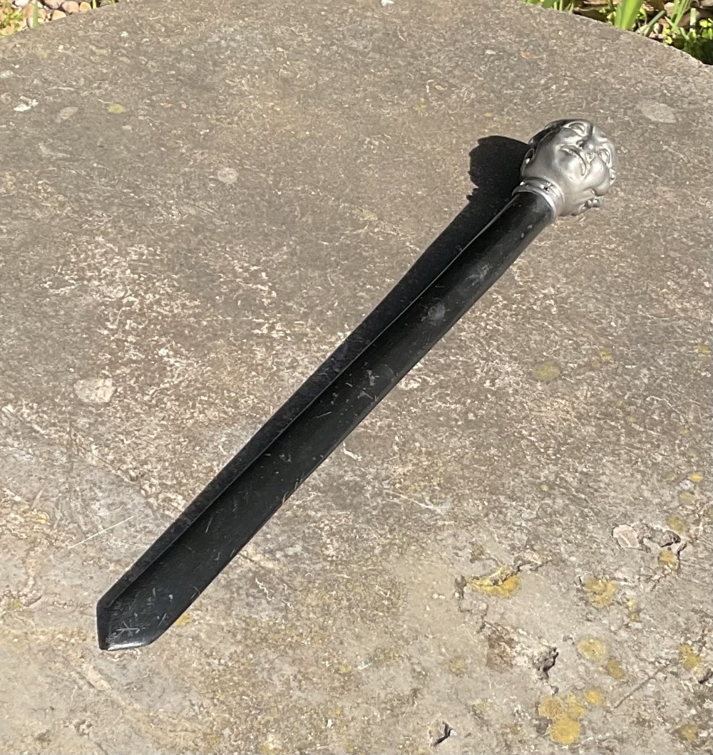 A Victorian page turner featuring a dark wooden blade attached to a pewter pommel carved with four distinct facial expressions.