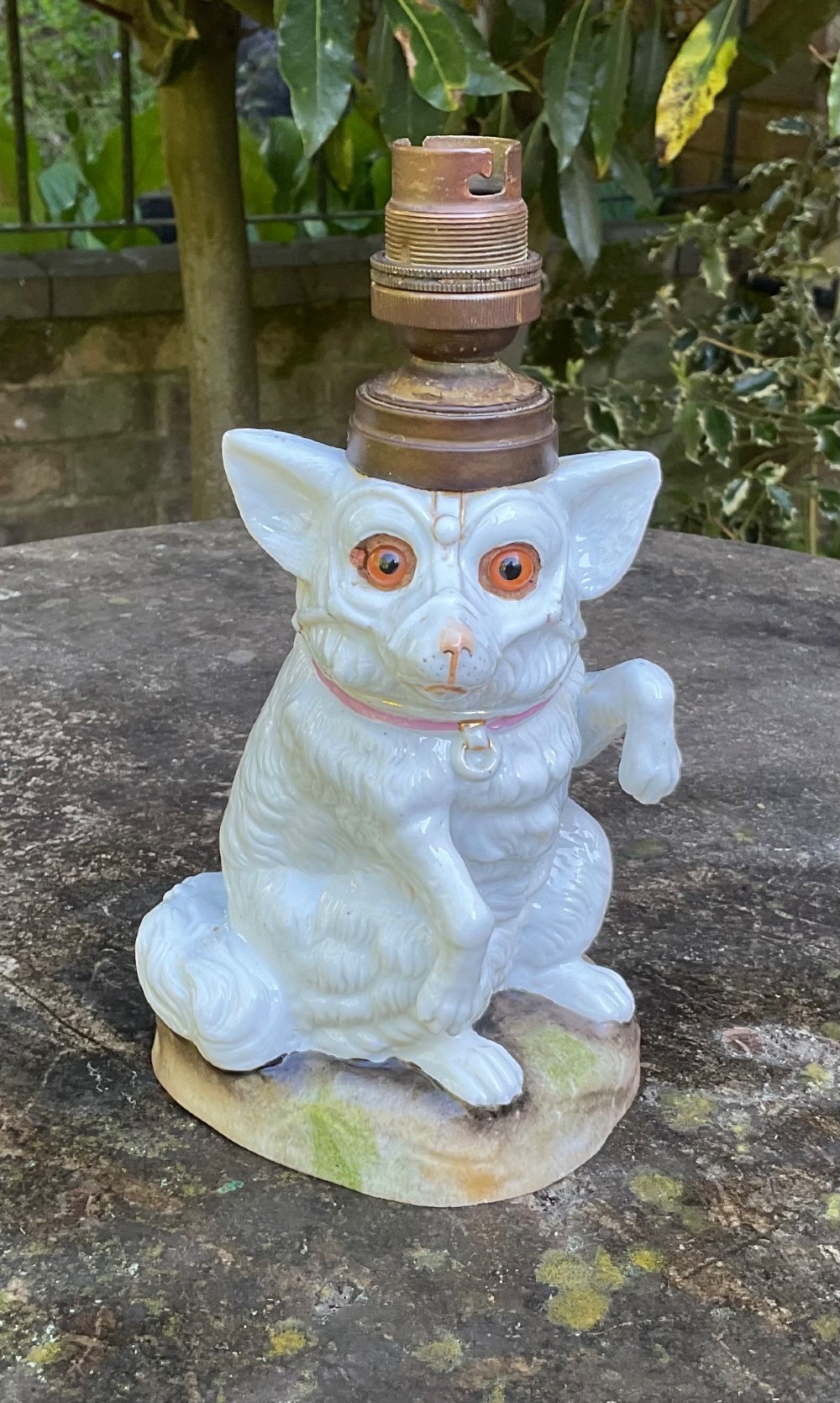 A late 19th-century German white glazed porcelain lamp base sculpted as a seated Spitz dog with orange glass eyes and a brass bulb fitment atop its head.