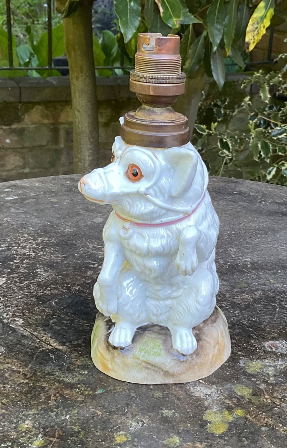 A late 19th-century German white glazed porcelain lamp base sculpted as a seated Spitz dog with orange glass eyes and a brass bulb fitment atop its head. View II