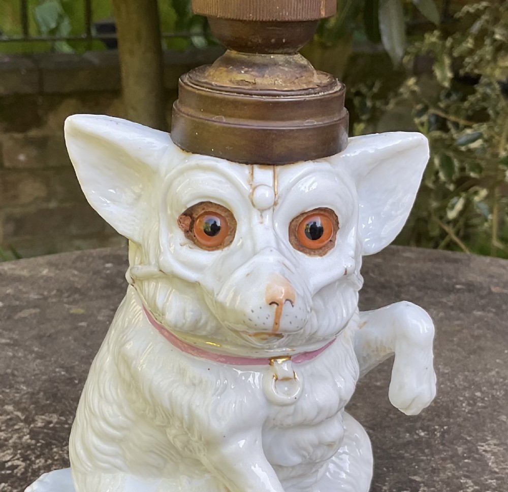 A late 19th-century German white glazed porcelain lamp base sculpted as a seated Spitz dog with orange glass eyes and a brass bulb fitment atop its head. View VI
