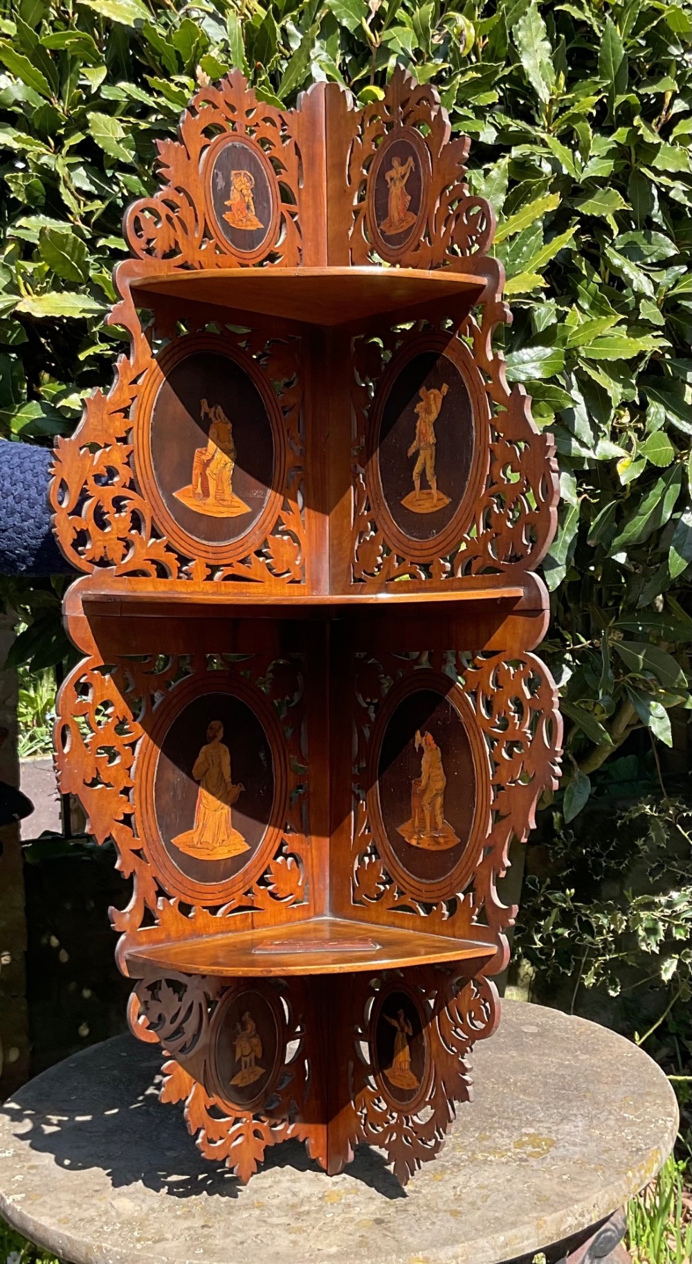 A Victorian three-tiered olive wood corner shelf with pierced fretwork edges and oval inlaid marquetry panels depicting Italian figures.