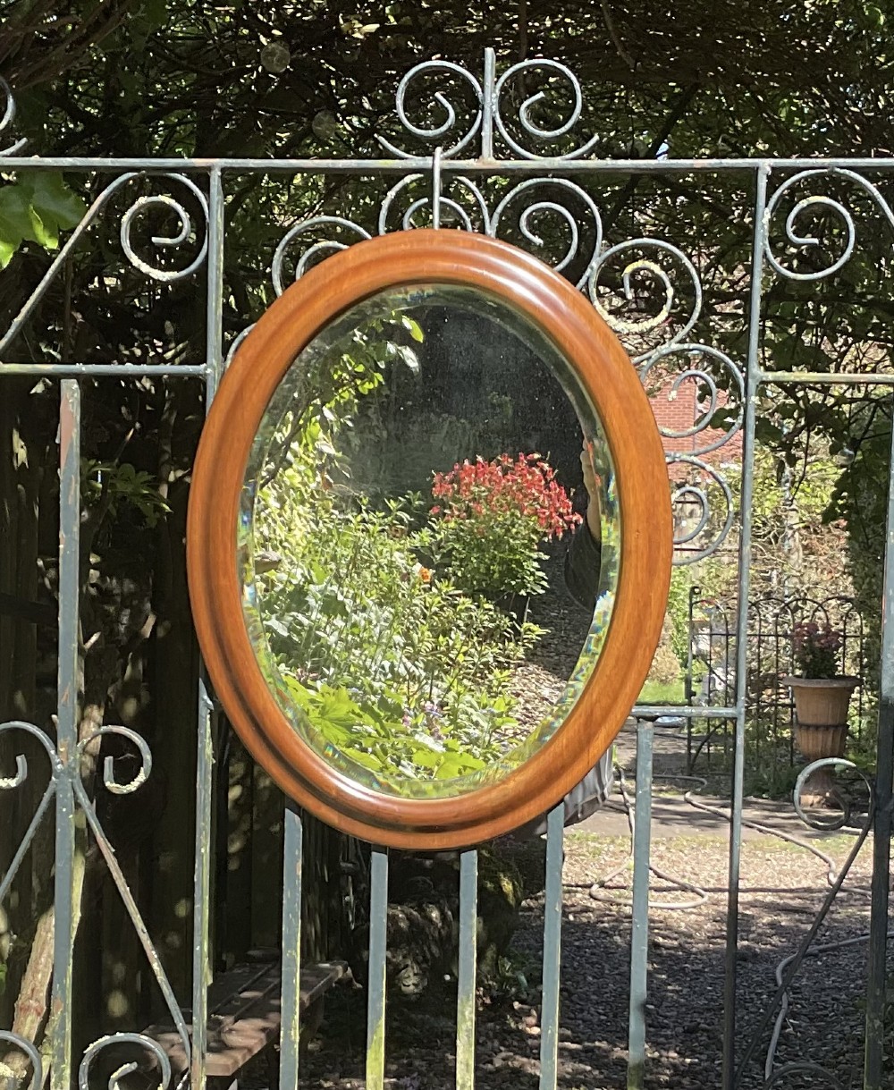 An Edwardian oval wall mirror set within a moulded mahogany timber frame featuring bevelled edge glass.