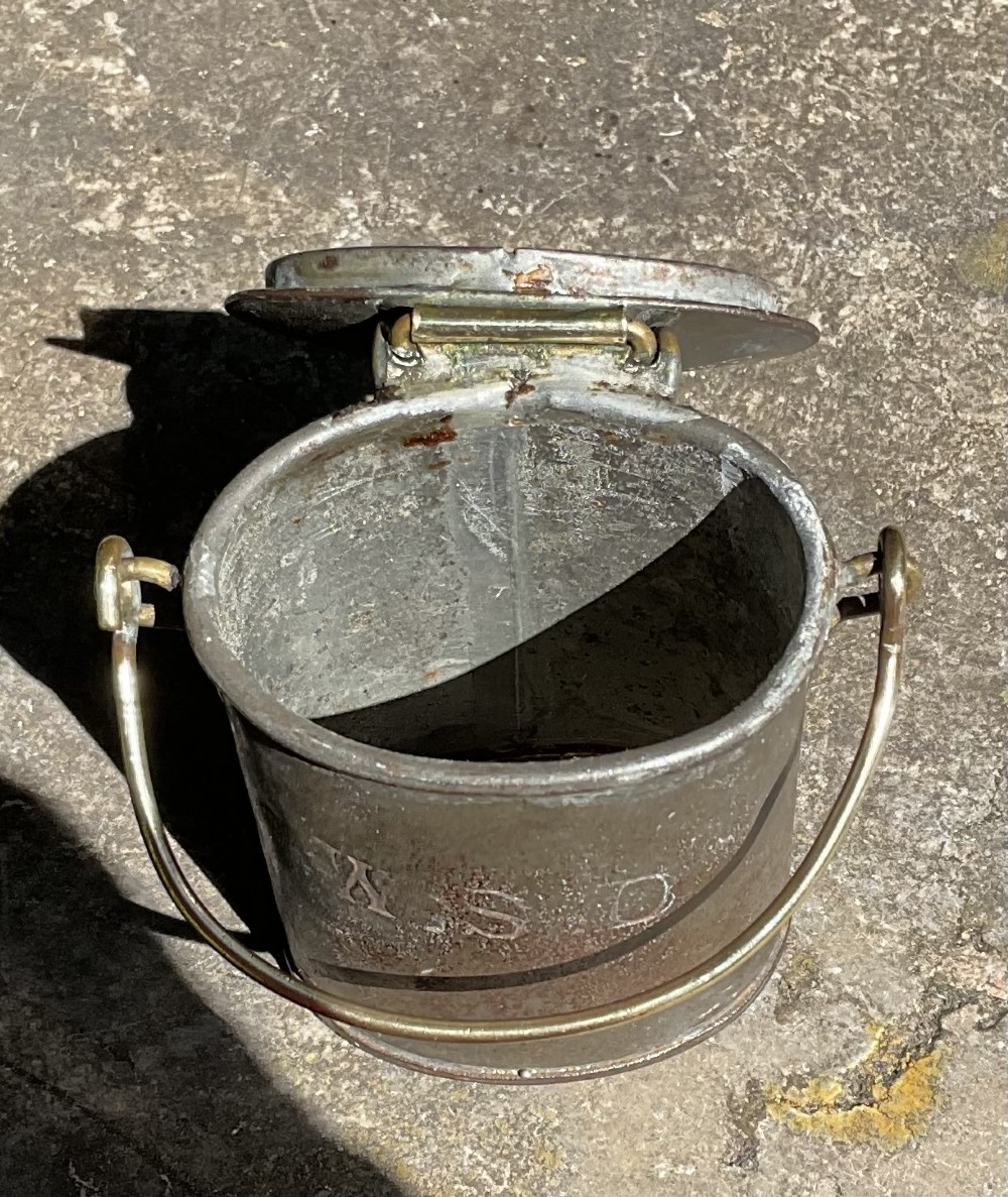 An antique metal dairy cream can featuring a brass swing handle, stamped lid lettering, and a hinged spout cover. View V