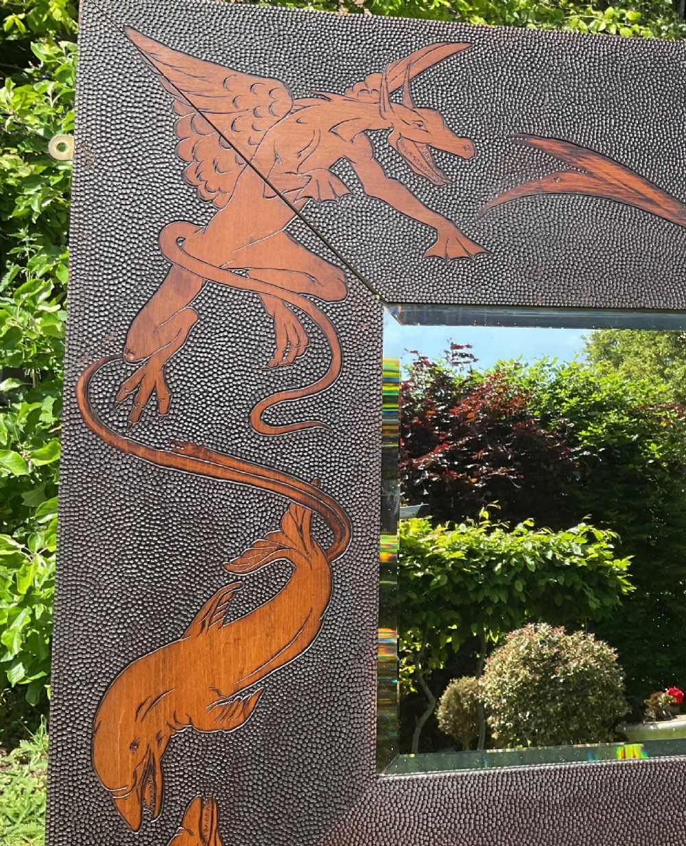 A large rectangular Arts and Crafts style wall mirror featuring a bevelled glass plate surrounded by a textured frame decorated with mythical dragons and dolphins. View II