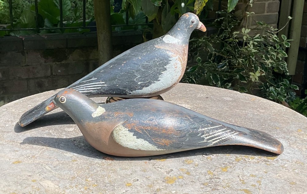 A pair of hand-carved and painted wooden pigeon decoys dating to circa 1900, showing grey and terracotta tones with worn patina.