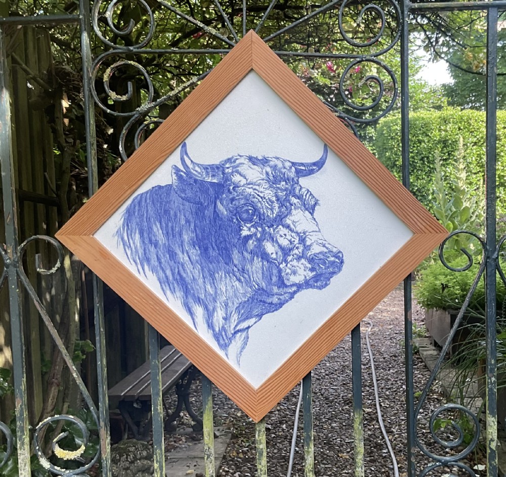 An Edwardian diamond-shaped Mintons ceramic tile mounted in a wooden frame depicting a detailed blue transfer print of a bull head.