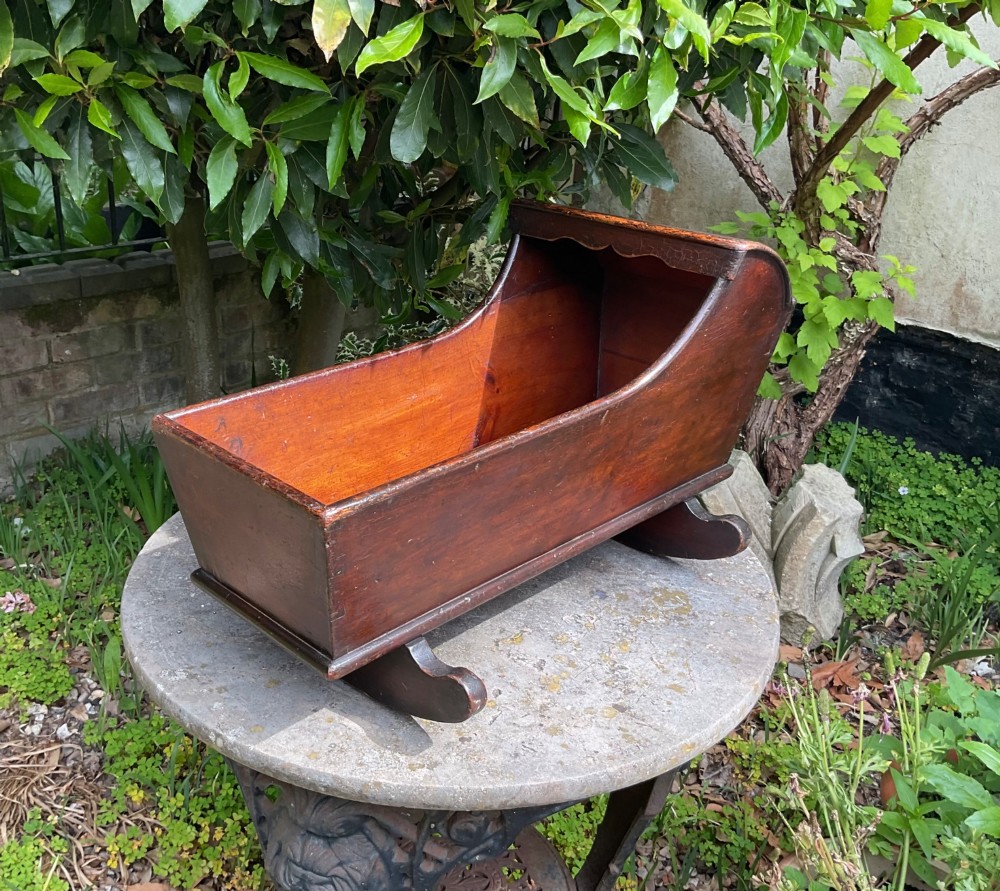 A Georgian pine miniature doll cradle featuring a hooded canopy, scalloped front moulding, and curved wooden rockers in a warm brown finish.