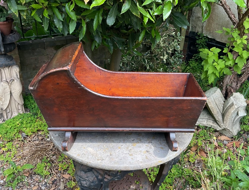 A Georgian pine miniature doll cradle featuring a hooded canopy, scalloped front moulding, and curved wooden rockers in a warm brown finish. View III