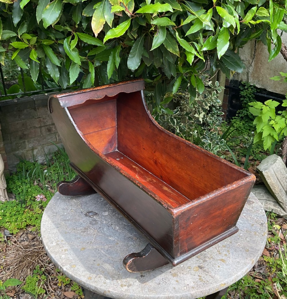 A Georgian pine miniature doll cradle featuring a hooded canopy, scalloped front moulding, and curved wooden rockers in a warm brown finish. View IV