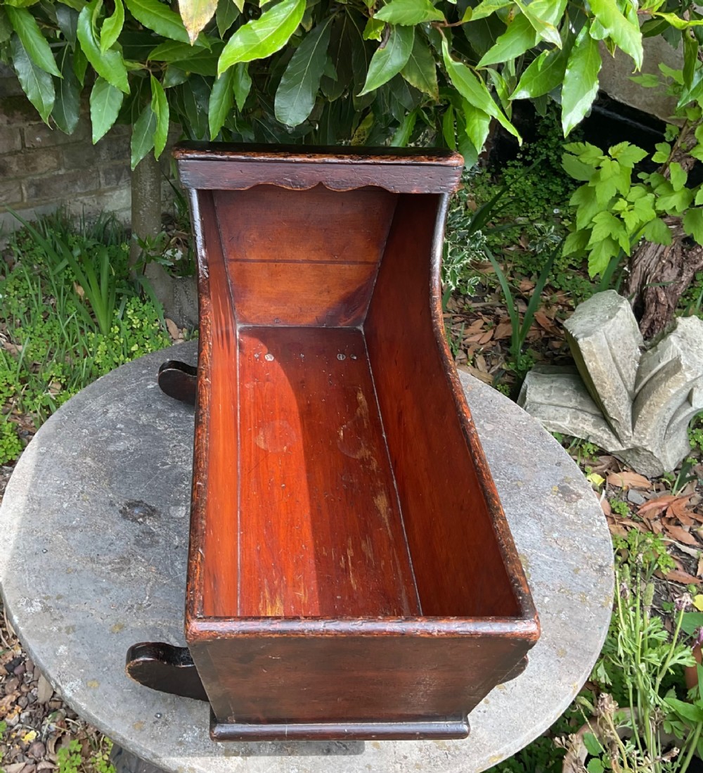 A Georgian pine miniature doll cradle featuring a hooded canopy, scalloped front moulding, and curved wooden rockers in a warm brown finish. View VII