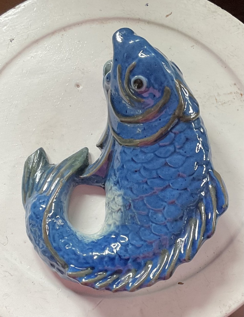 A glazed earthenware wall pocket modelled in the form of a fish with blue scales, green fins, and an open mouth vessel. View II