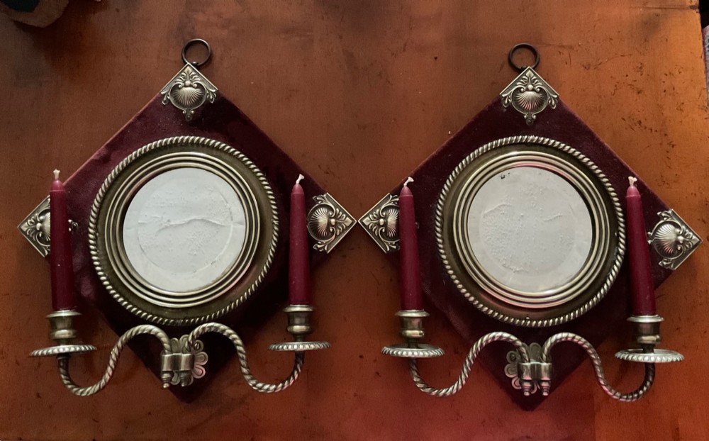 A pair of diamond-shaped Victorian girandole mirrors featuring burgundy velvet fabric, brass shell corner mounts, circular mirrors, and twin brass candle branches.