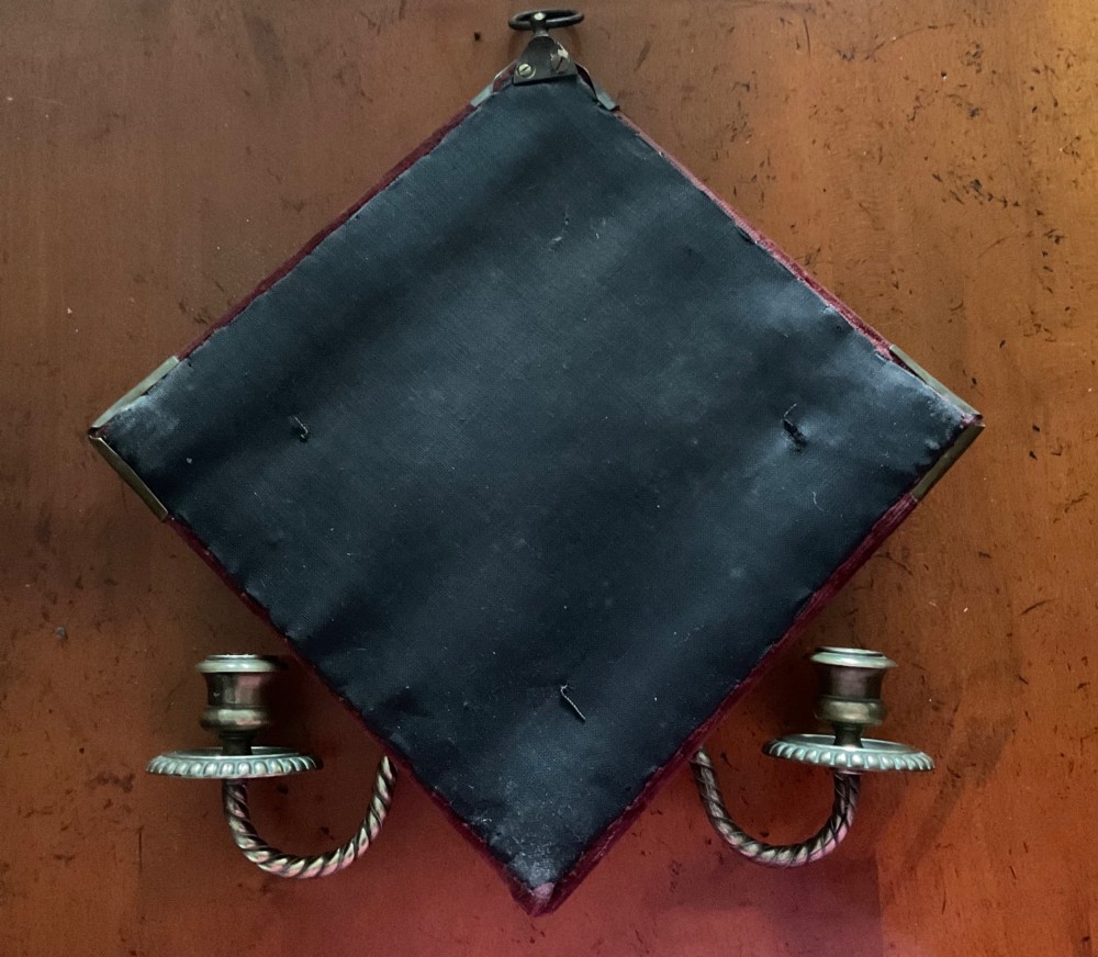 A pair of diamond-shaped Victorian girandole mirrors featuring burgundy velvet fabric, brass shell corner mounts, circular mirrors, and twin brass candle branches. View V