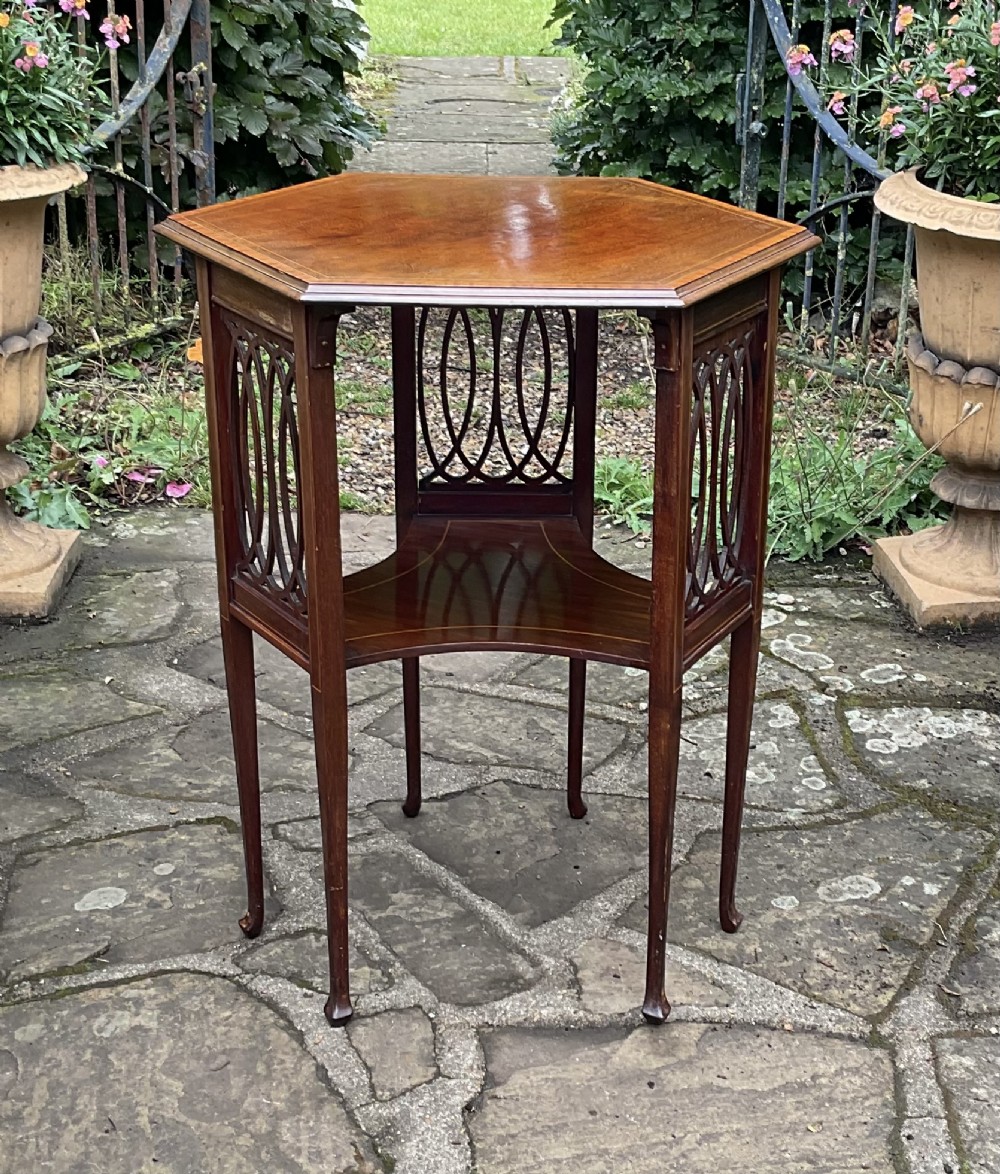 An Edwardian octagonal mahogany lamp table featuring line inlay, a concave lower shelf, and pierced oval fretwork side panels.