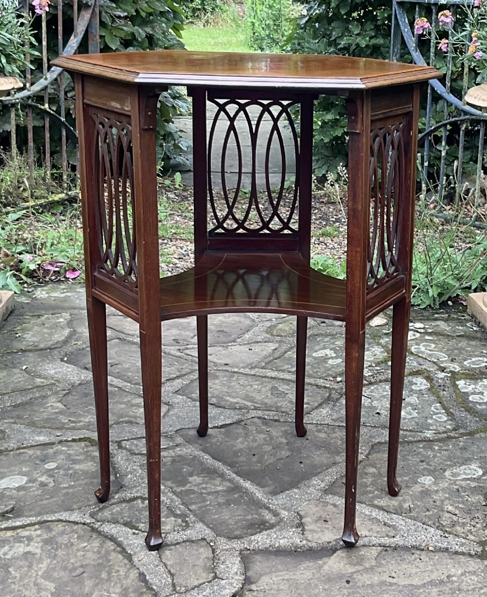 An Edwardian octagonal mahogany lamp table featuring line inlay, a concave lower shelf, and pierced oval fretwork side panels. View V