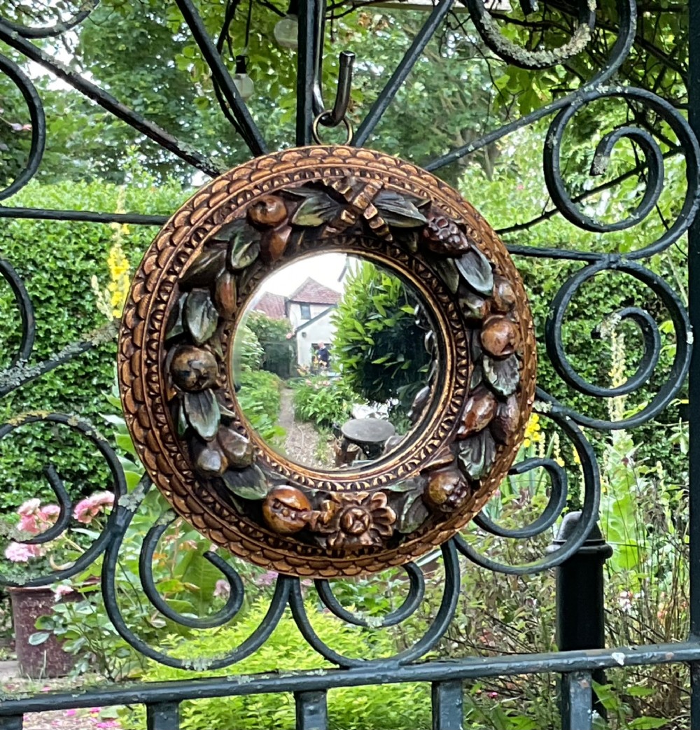 A circular carved wood convex wall mirror featuring a relief fruit and foliage wreath frame with a gilded finish.